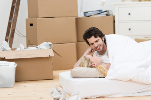 Loving couple sleeping on the floor on a mattress surrounded by cardboard boxes after moving like a Pro San Diego Mover