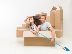 young couple sitting in a box pretending they are in a boat, paddeling with a broom